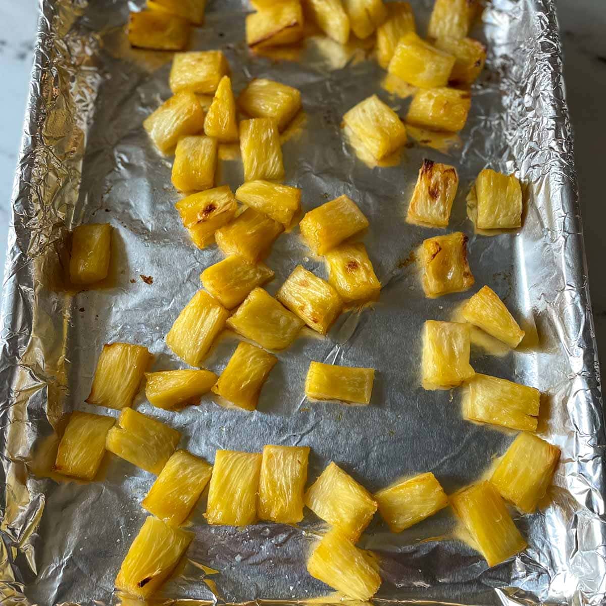 Roasted pieces of pineapple sit on a sheet tray lined with tin foil.