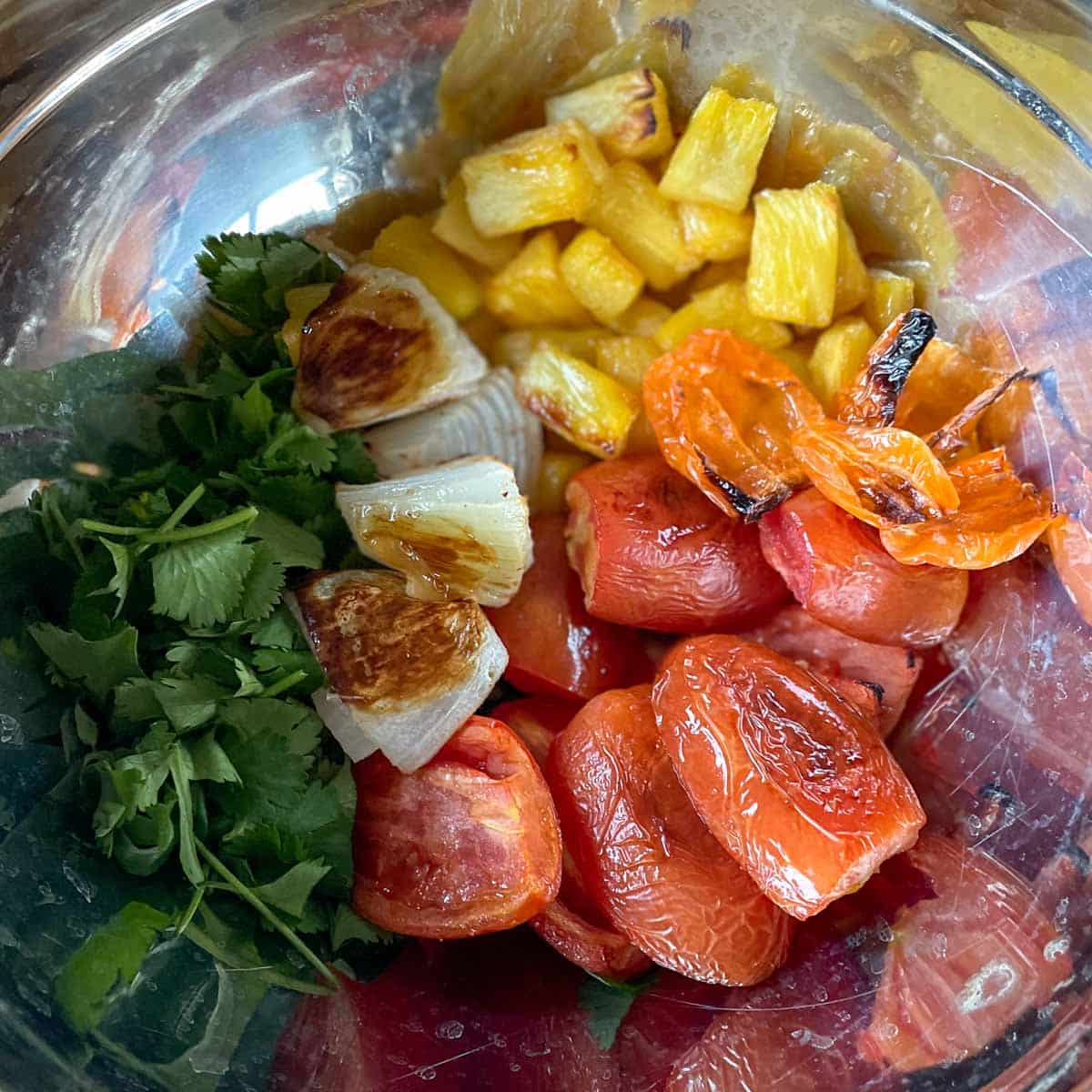 The roasted ingredients for pineapple habanero salsa are shown in a metal bowl.