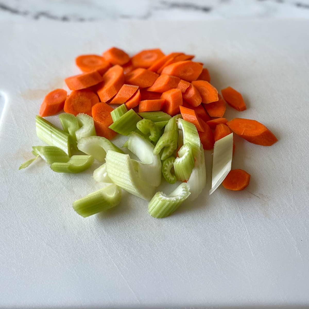 Sliced carrots and celery sit on a white cutting board.
