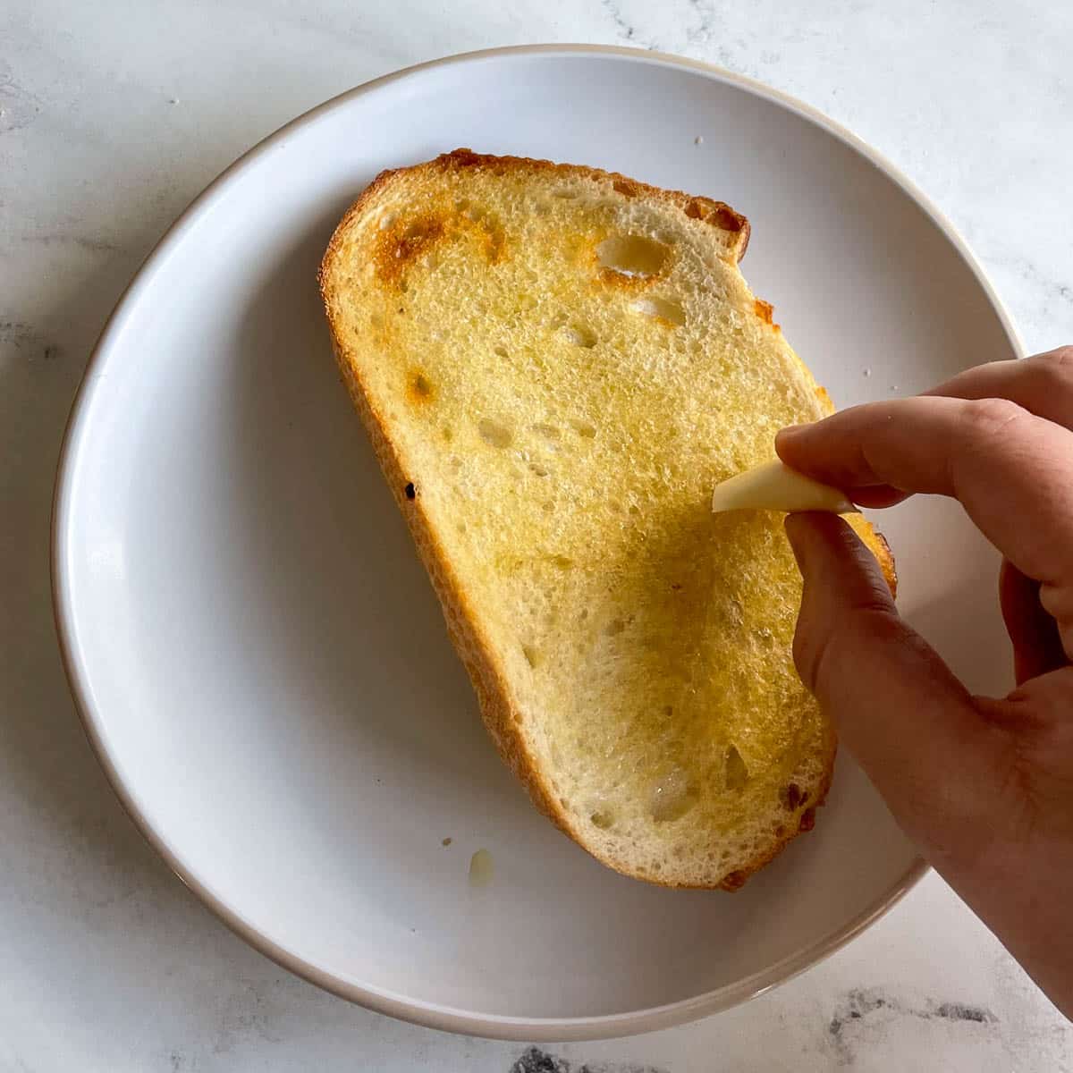 A piece of toasted bread is rubbed with a clove of garlic.