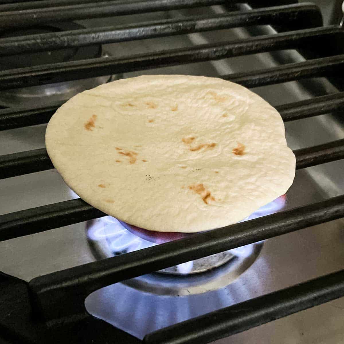 A flour tortilla sits over the flame of a gas burner.