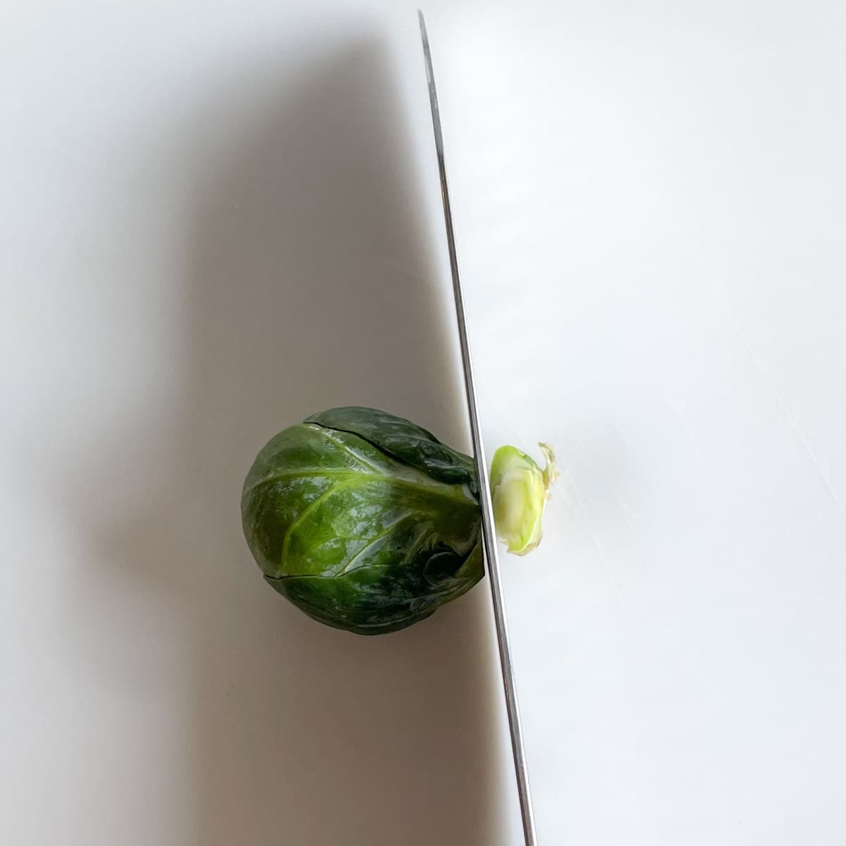 The base of a brussels sprouts is cut off with a kitchen knife.