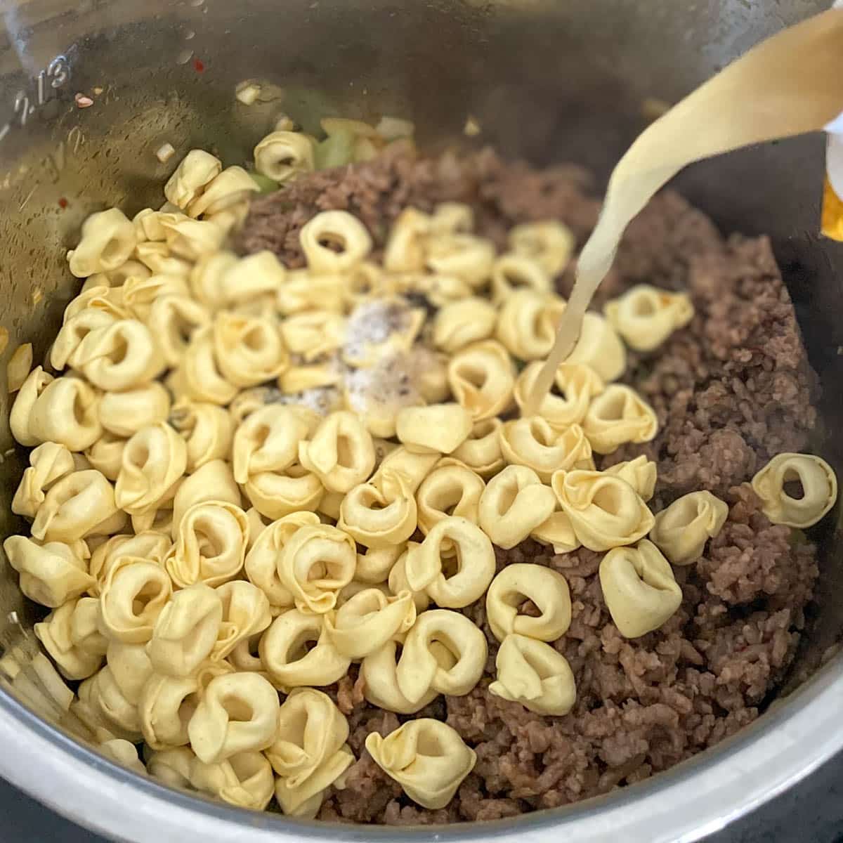 Tortellini, seasonings, sausage, and broth is added to the soup ingredients.