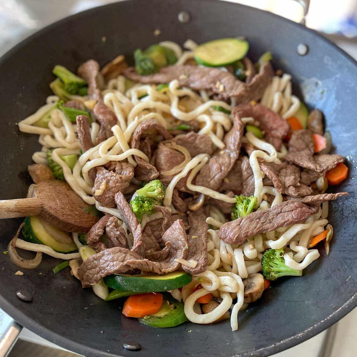 Cooked beef is added into the noodles and vegetables in the wok.