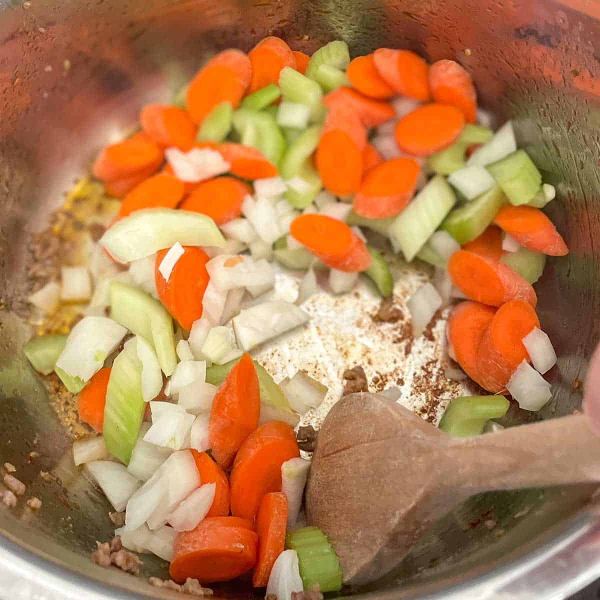 Carrot, celery, and onion are stirred in the Instant Pot.