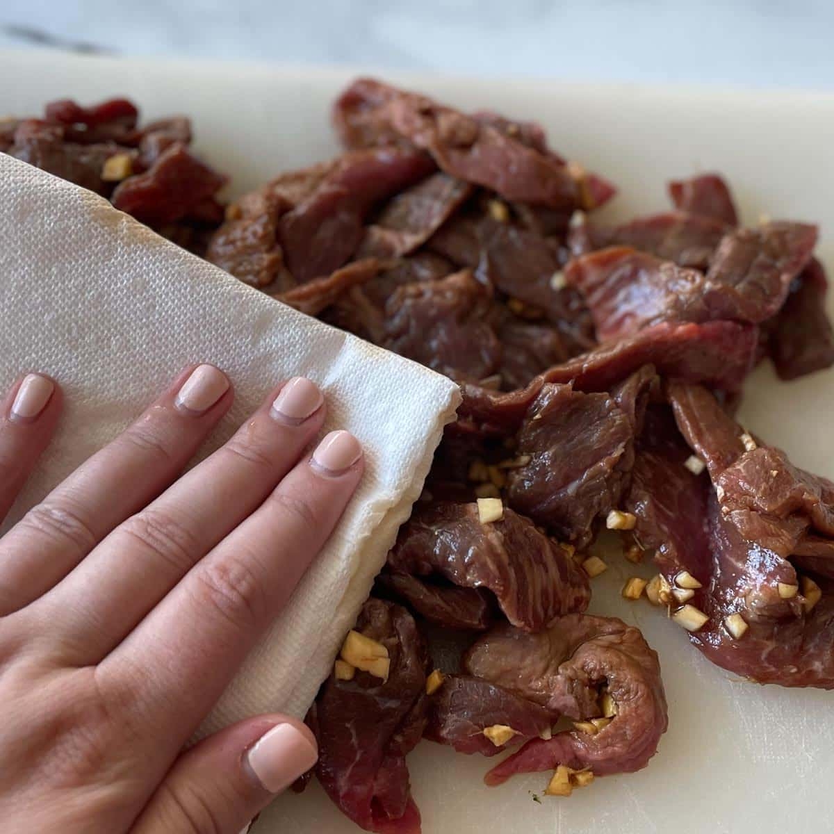 The marinated beef is patted dry on a cutting board.