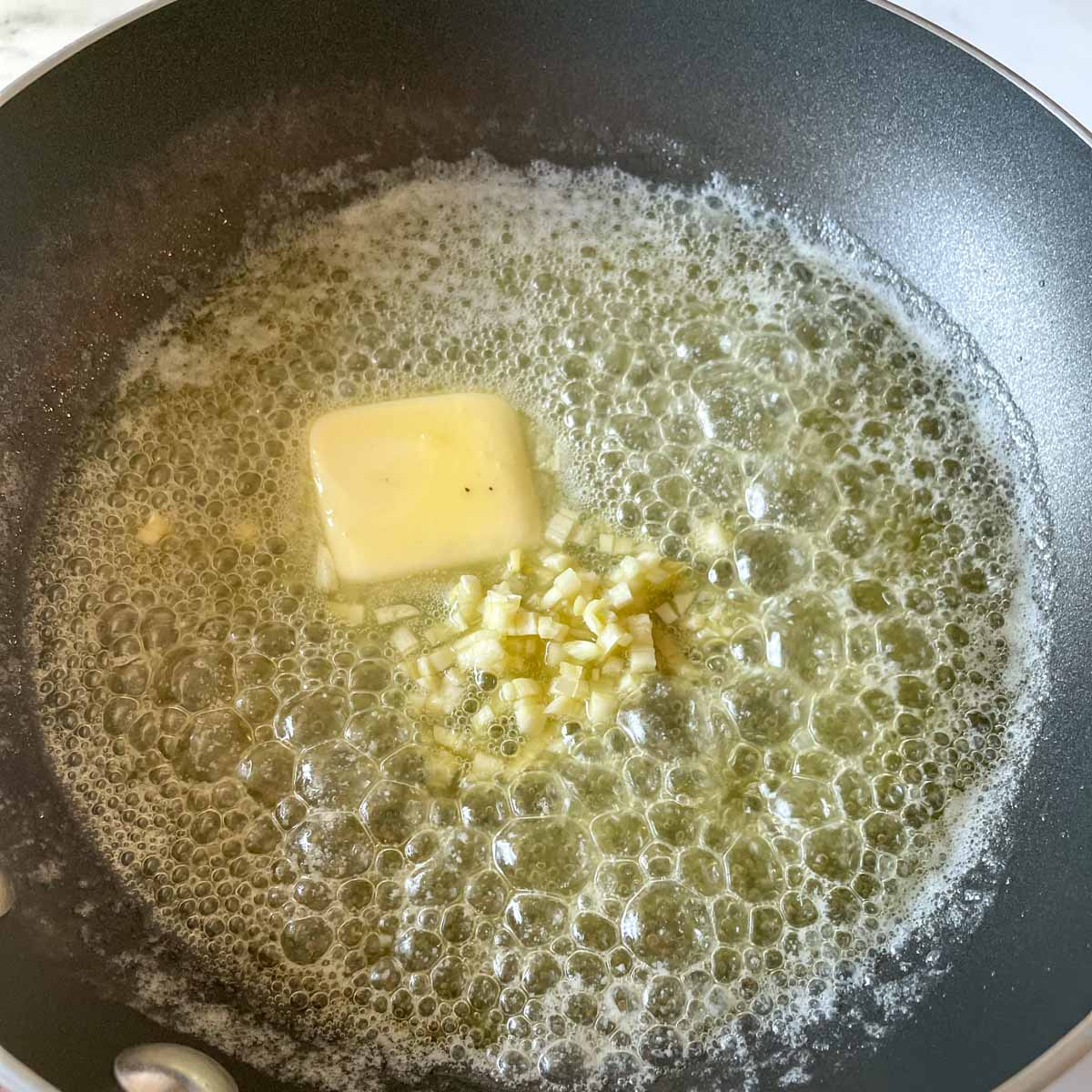 Chopped garlic is added to the melted butter in a black pan.