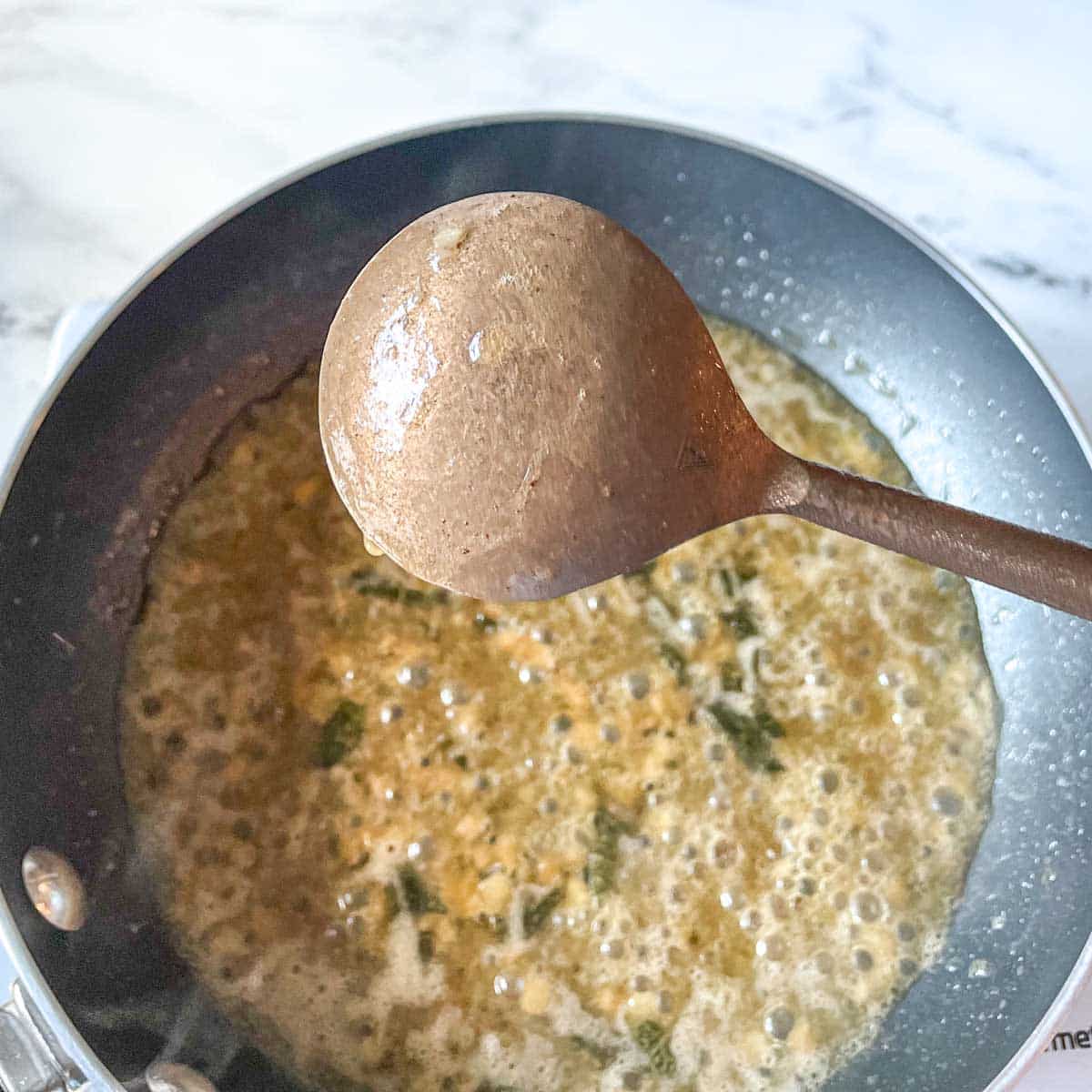 Lobster ravioli sauce is shown coating the back of a spoon with the sauce simmering in the background.