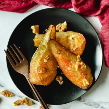 Air fryer pears sit on a black plate topped with walnuts.