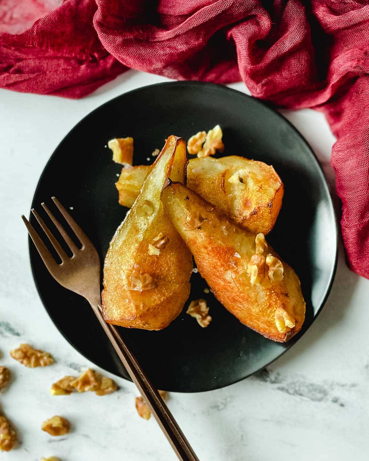 Air fryer pears sit on a black plate topped with walnuts.