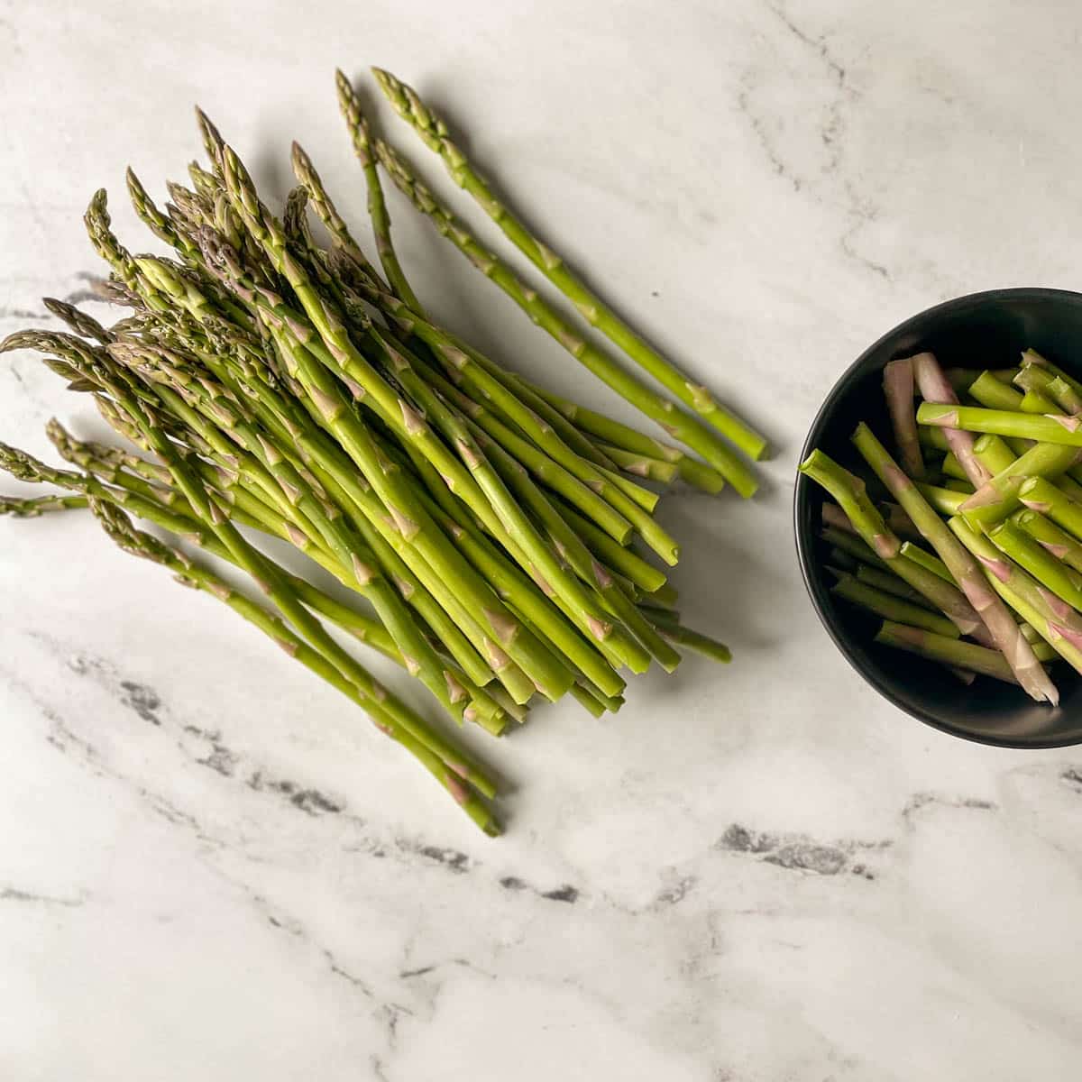 A bunch of trimmed asparagus sits on a white marble counter.