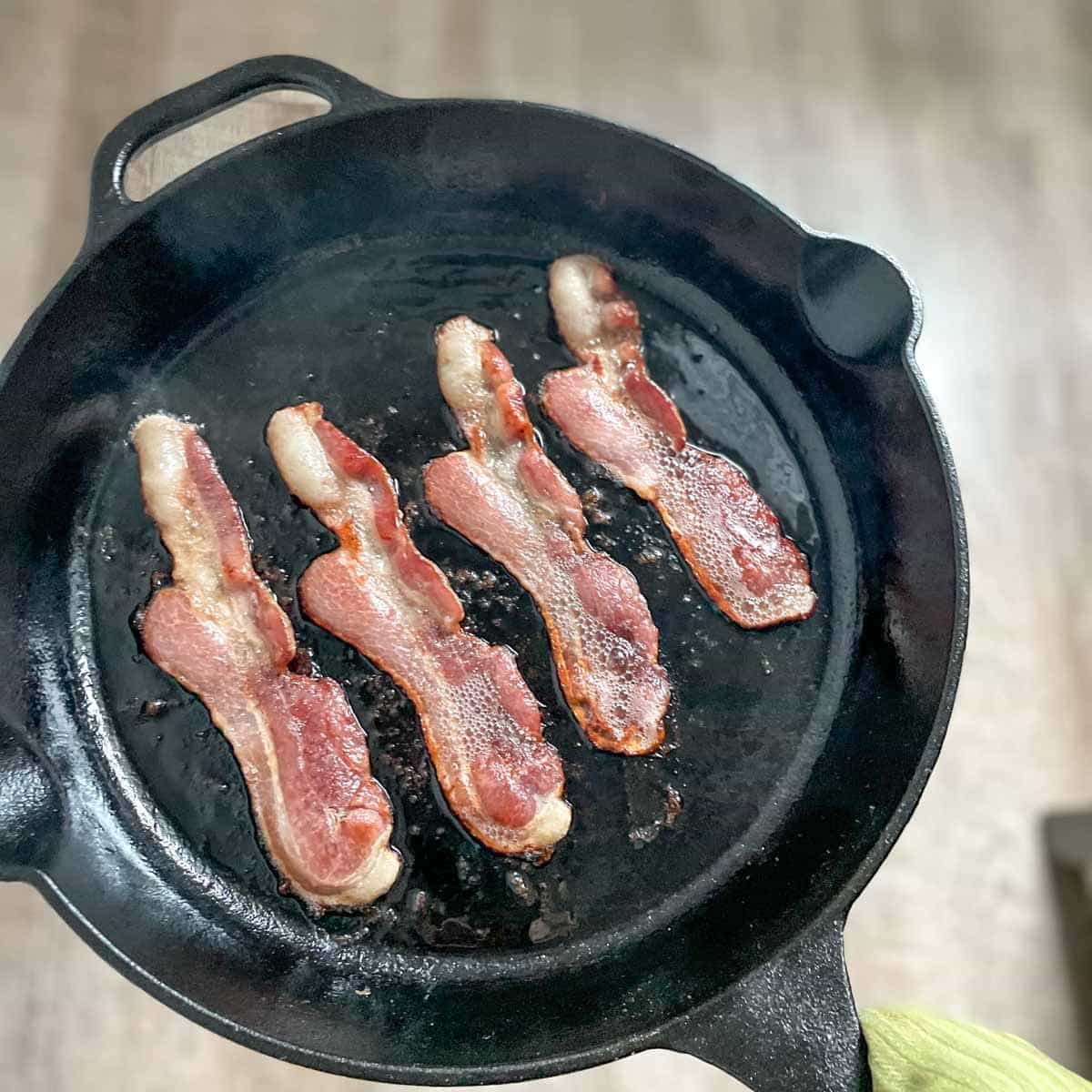 Bacon fries in a cast iron skillet.
