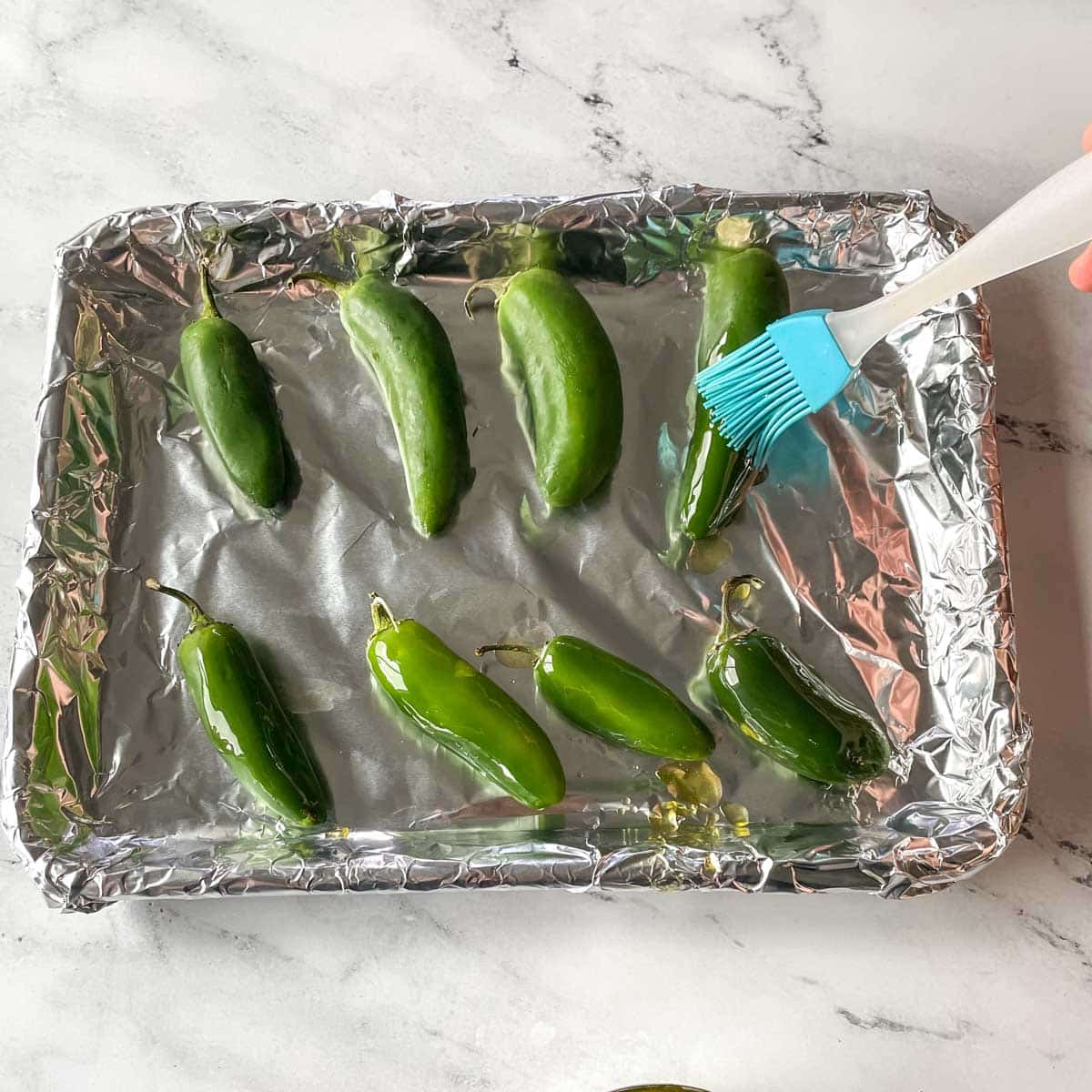 Jalapeños are basted in olive oil on a sheet tray lined with foil.