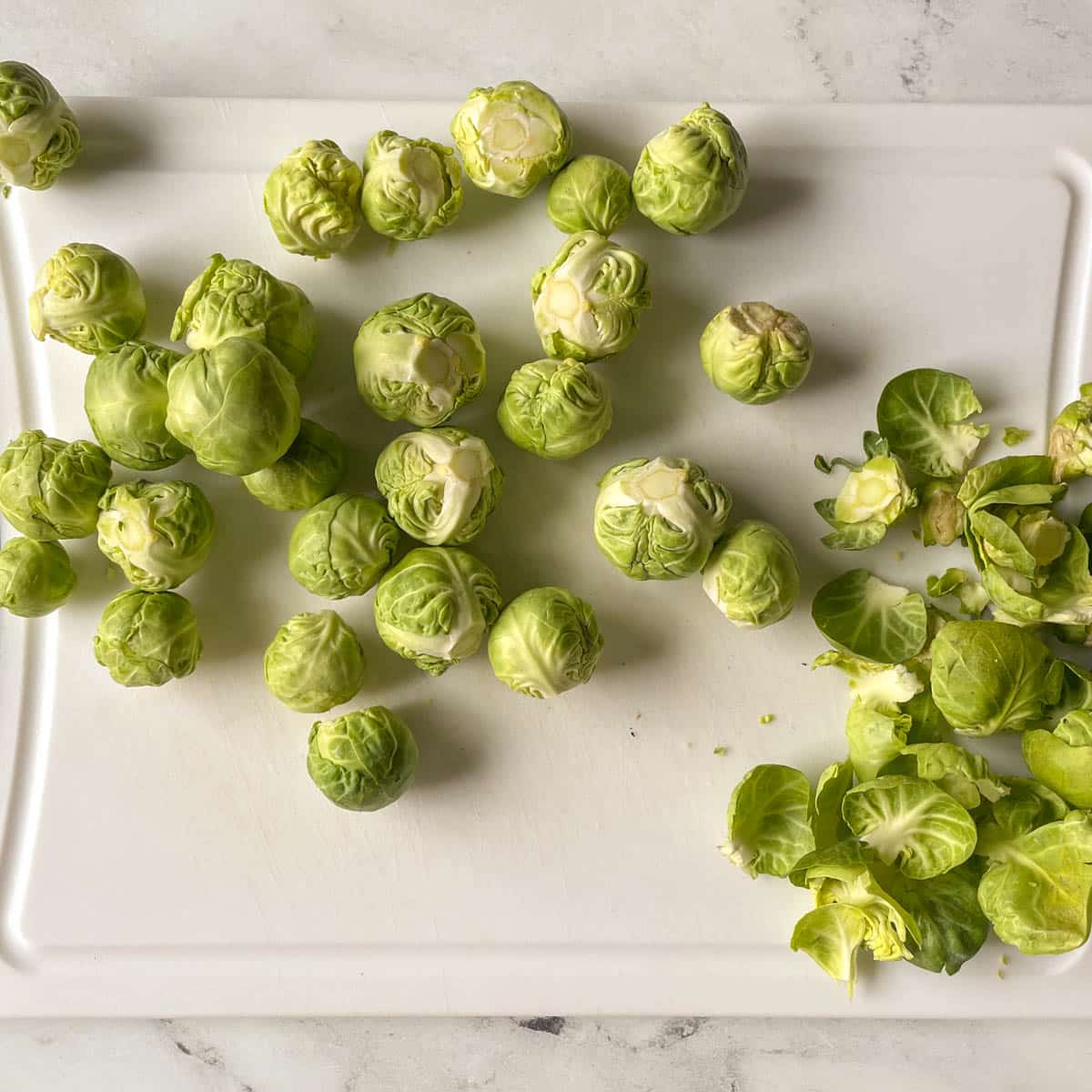 Trimmed brussels sprouts sit on a white cutting board.