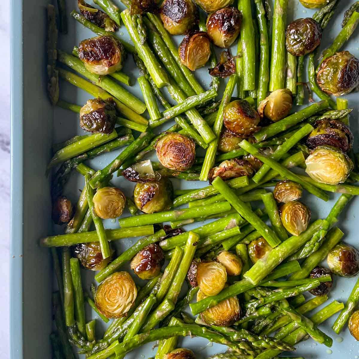Roasted brussels sprouts and asparagus sit on a blue sheet tray.