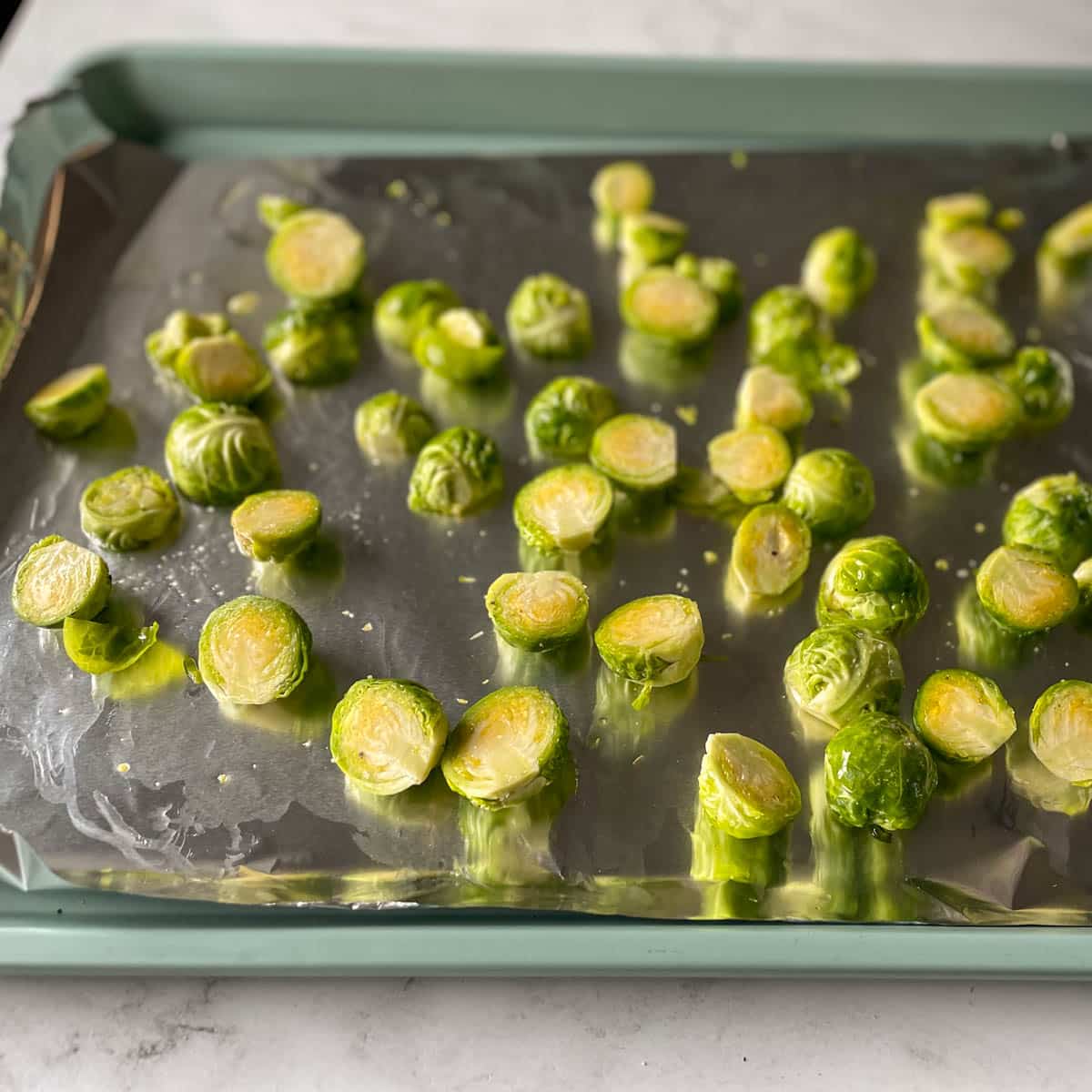 Halved brussels sprouts coated in oil and salt sit on on a sheet tray.