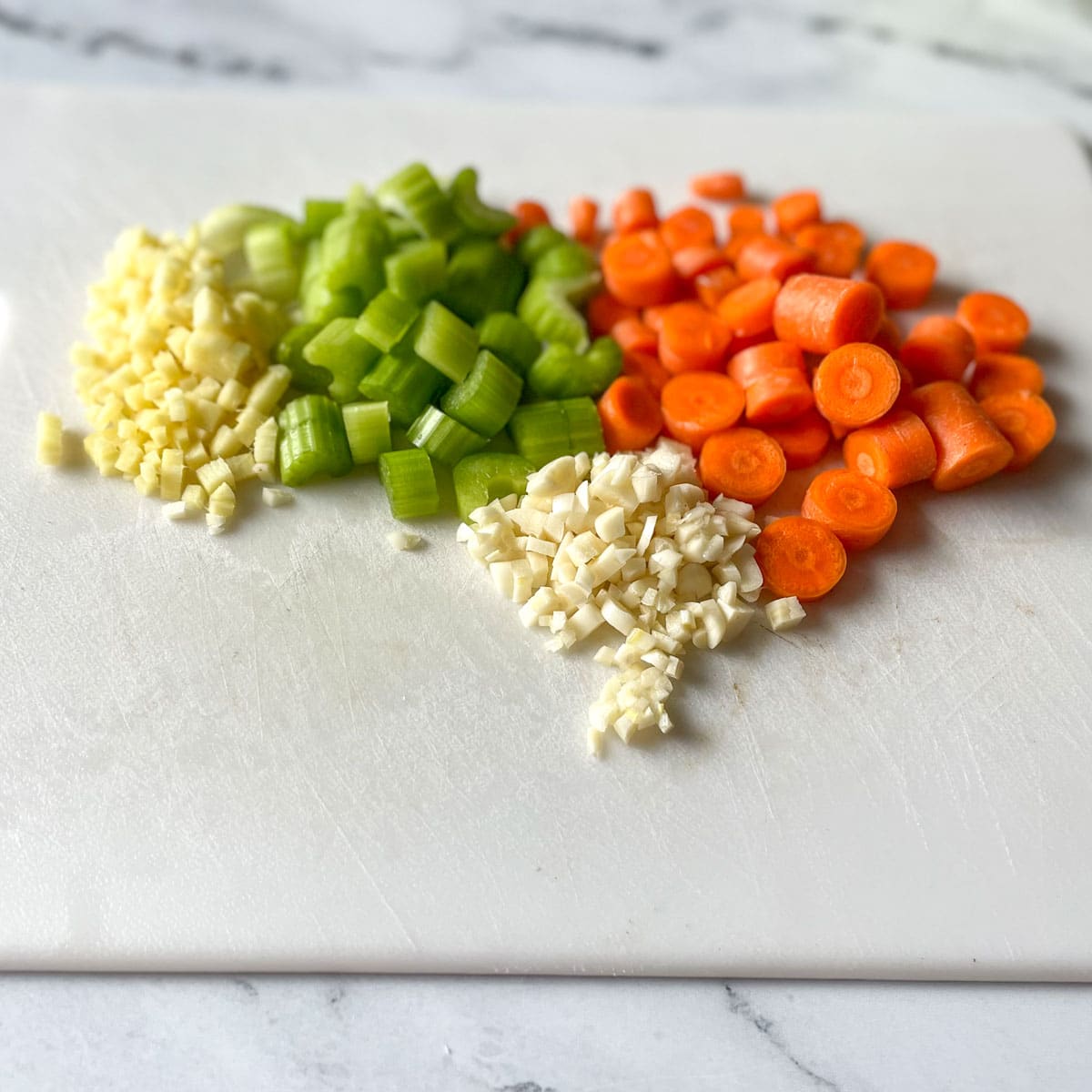 Chopped ginger, garlic, celery, and carrot sit on a white cutting board.