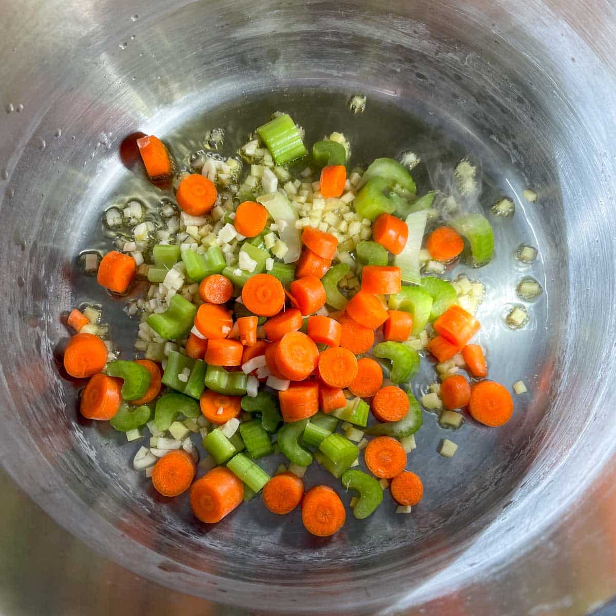 Ginger, garlic, celery, and carrot sweat in a pot.