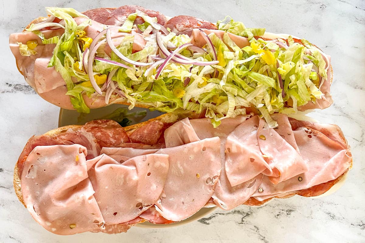 The dressed lettuce, onion, and pepperoncini is added to the grinder sandwich.