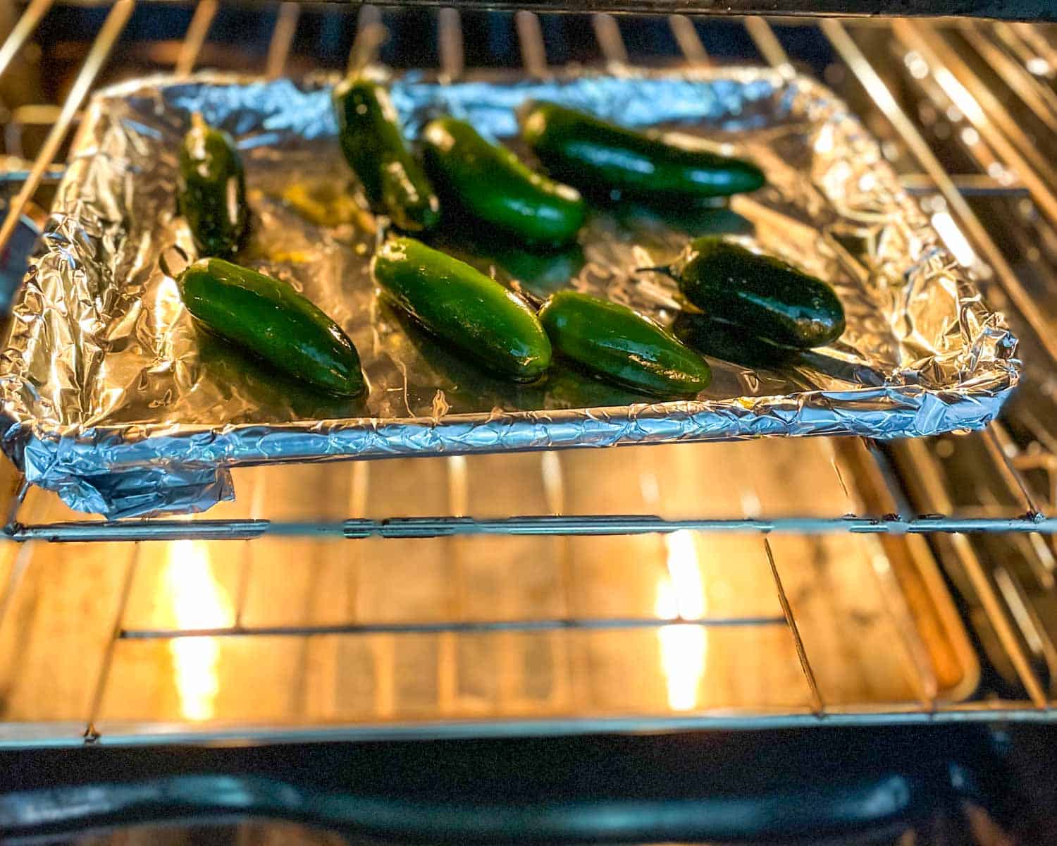 Jalapeños coated in olive oil on a lined sheet tray are moved to the oven.