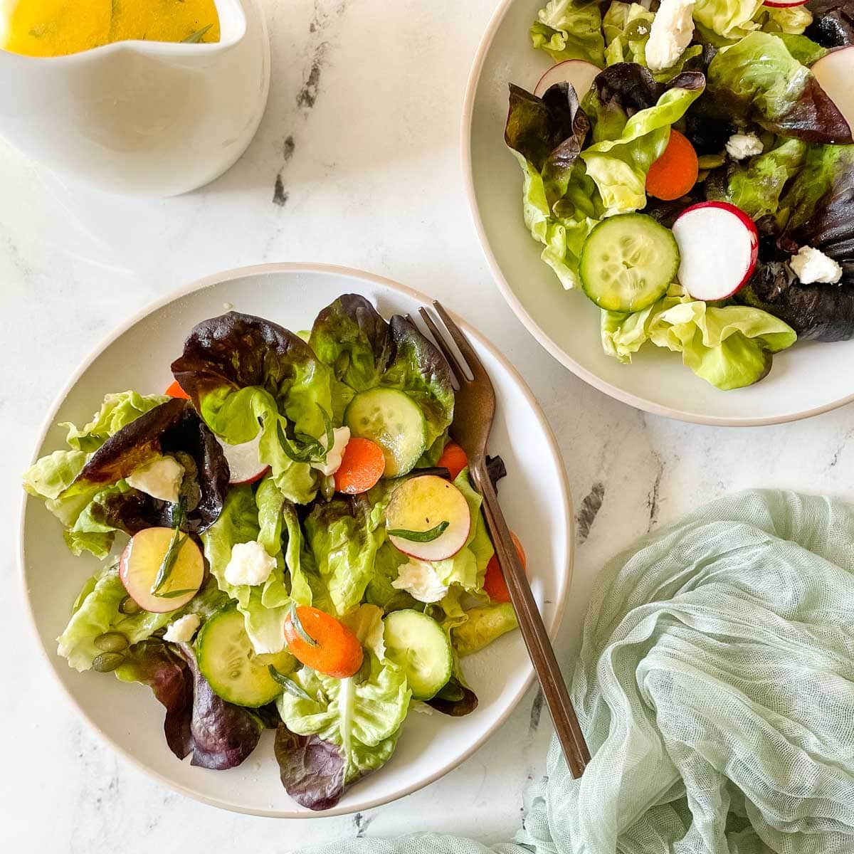 Two plates of side salad are shown dressing in a lemon herb vinaigrette.