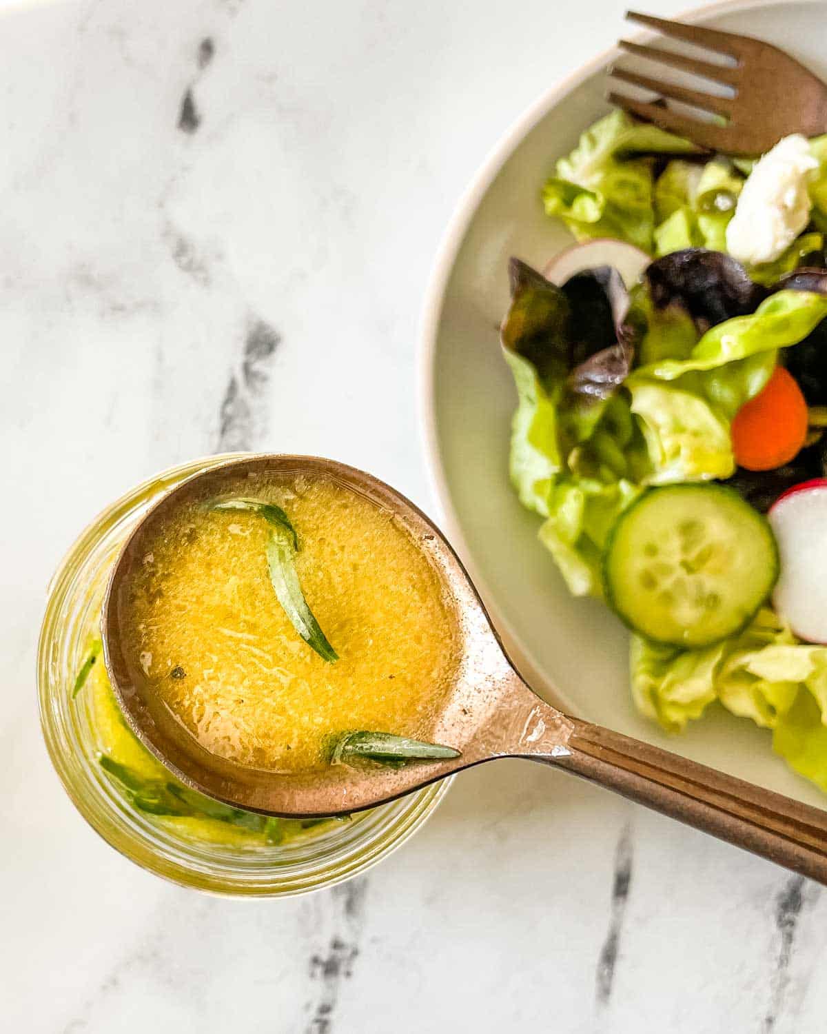 A spoonful of lemon herb vinaigrette is shown in the foreground over a green salad.