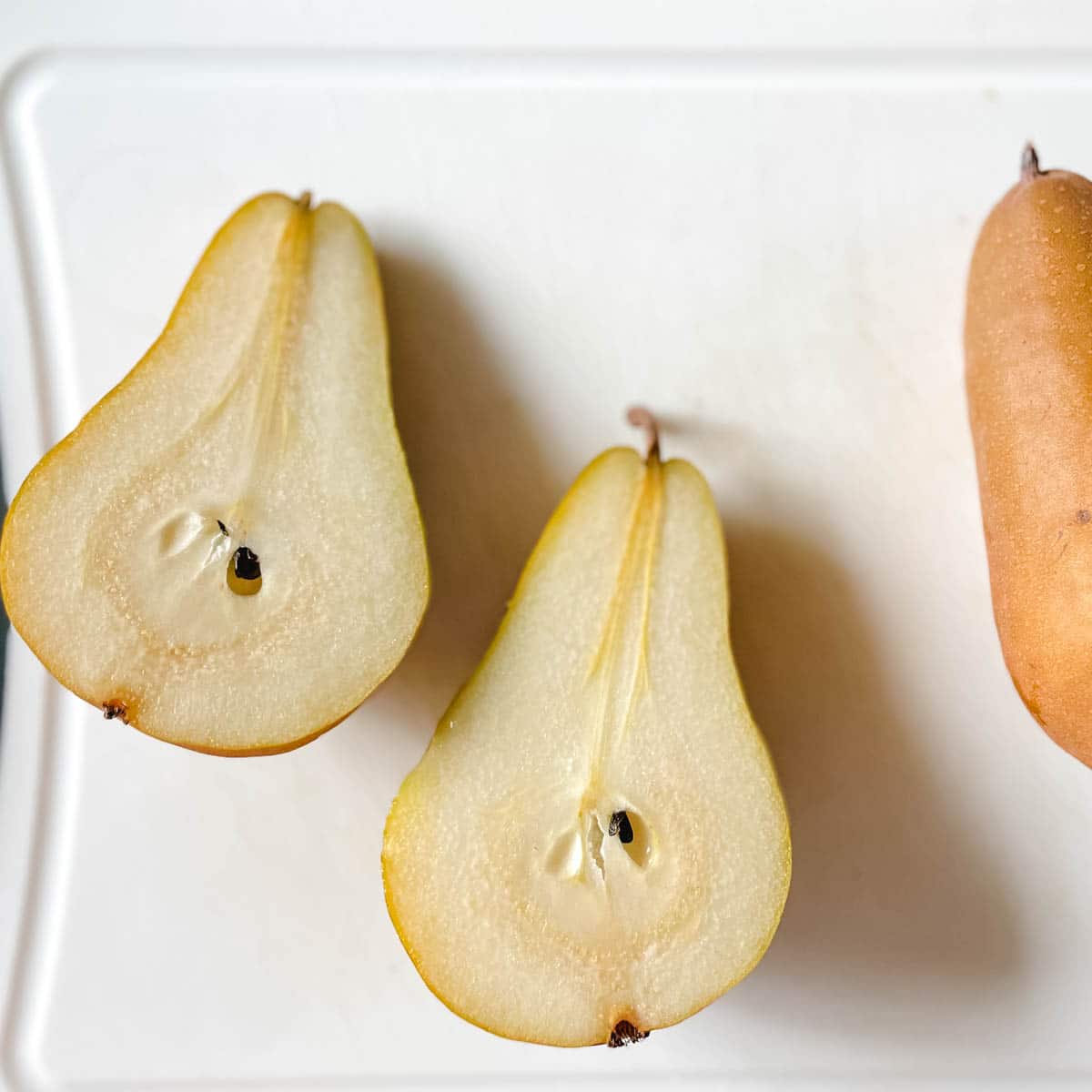 Image shows a halved pear on a white cutting board.