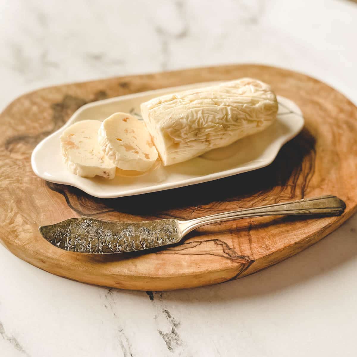 A log of roasted garlic butter is shown on a white butter dish with a butter knife.