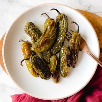 Roasted Jalapeños are shown on a white plate with a copper fork and a red linen.