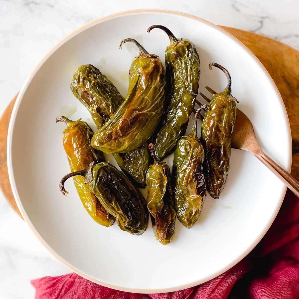 Roasted Jalapeños are shown on a white plate with a copper fork and a red linen.