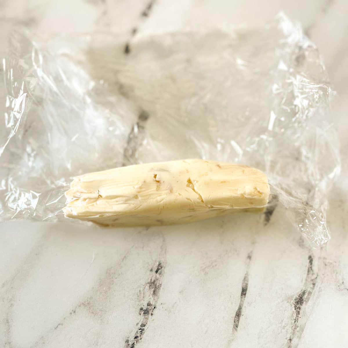 Roasted garlic butter is shaped into a log in a piece of plastic wrap.