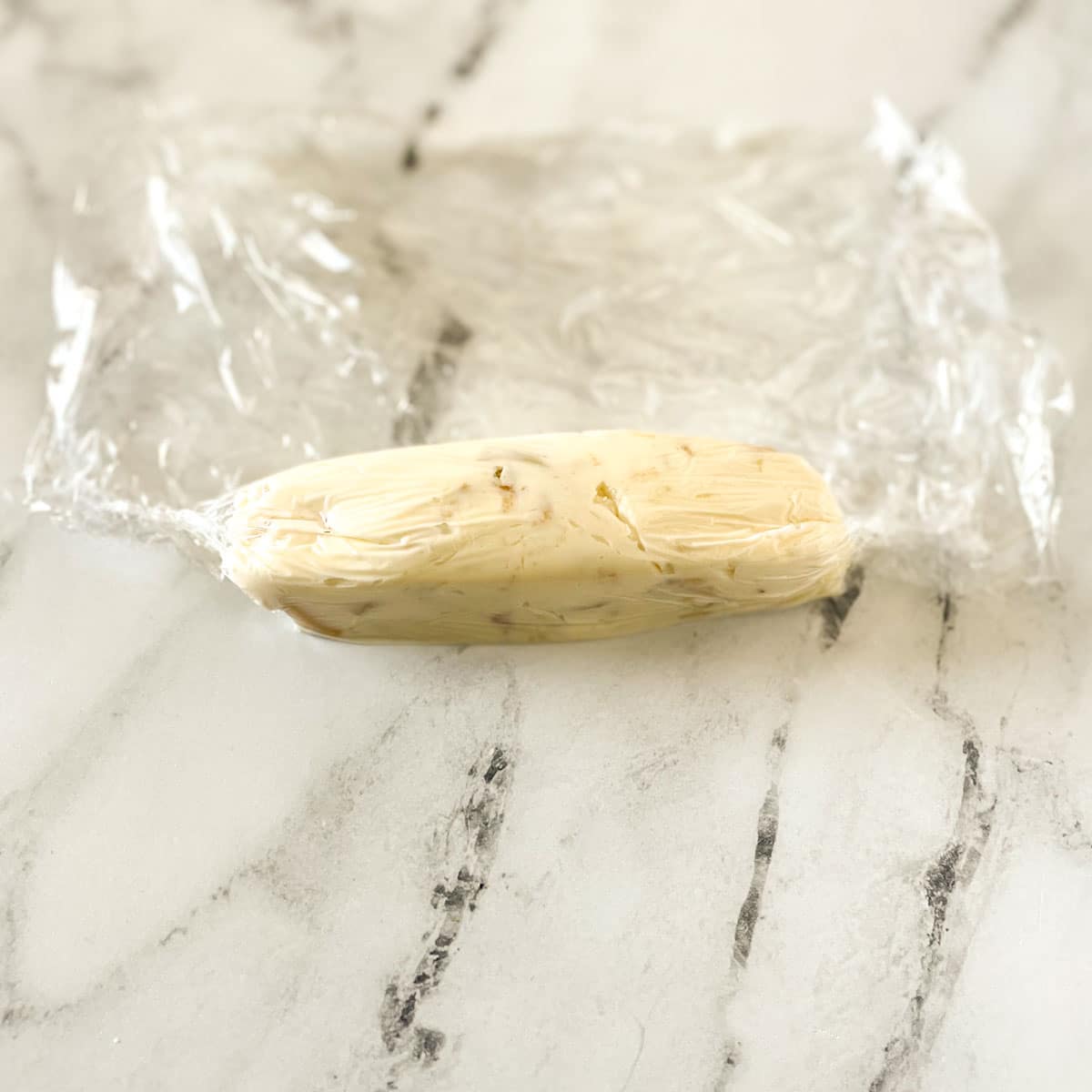 The edges of the plastic wrap around a log of roast garlic butter are cinched.