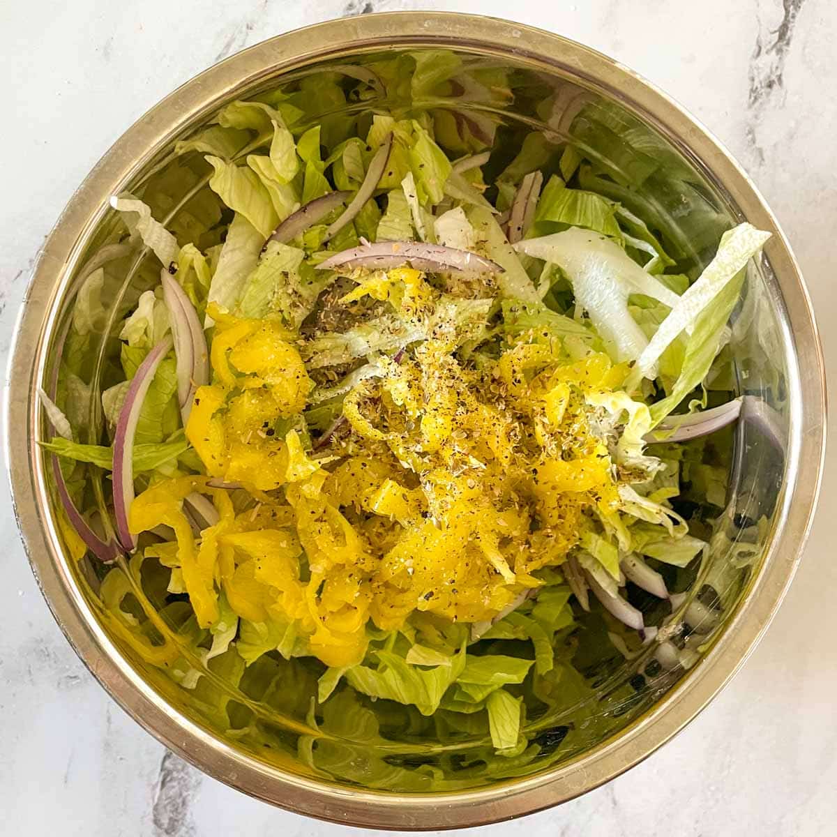 Lettuce, onion, pepperoncini, salt, pepper, garlic, red wine vinegar and olive oil is mixed in a bowl.