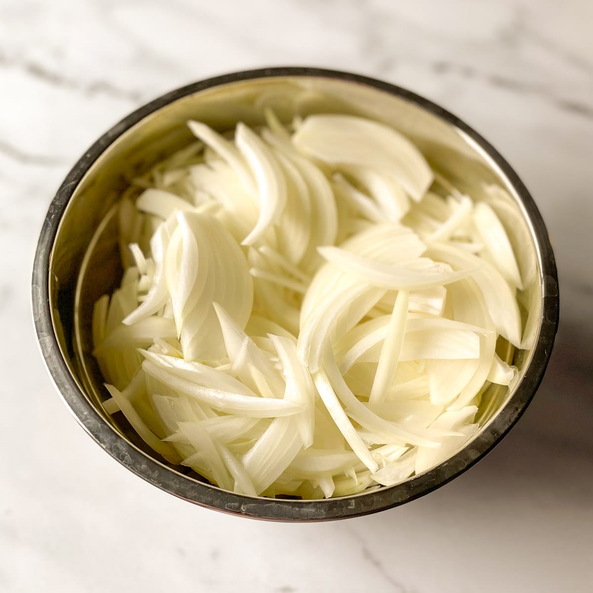 Sliced onions sit in a metal bowl.