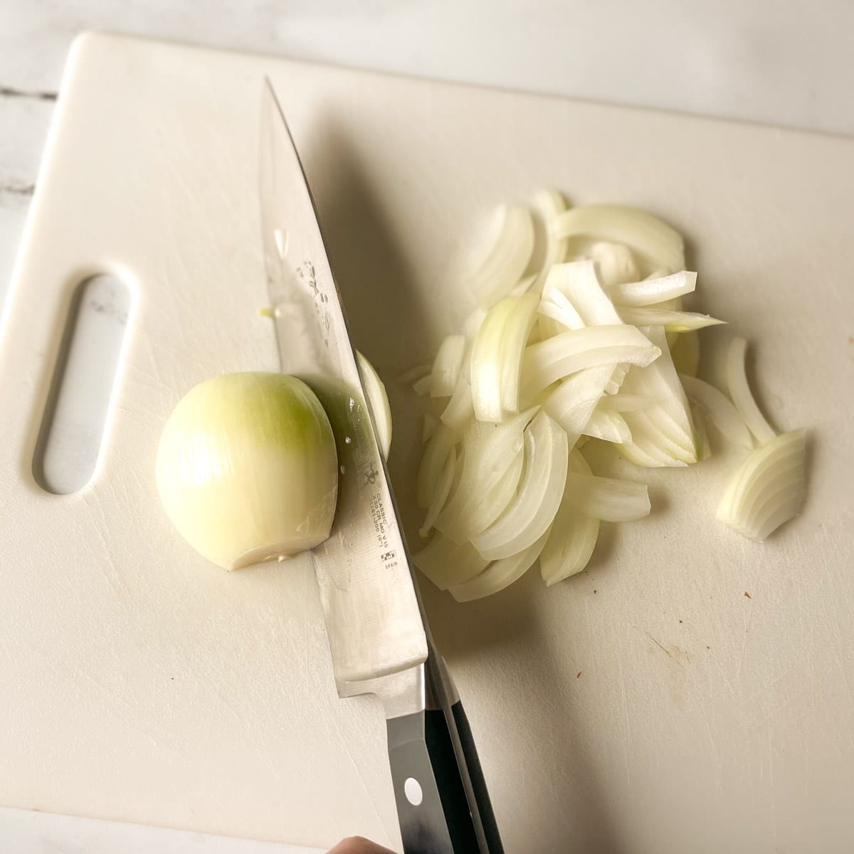 A halved onion is sliced at a diagonal angle to create even, thin slices.