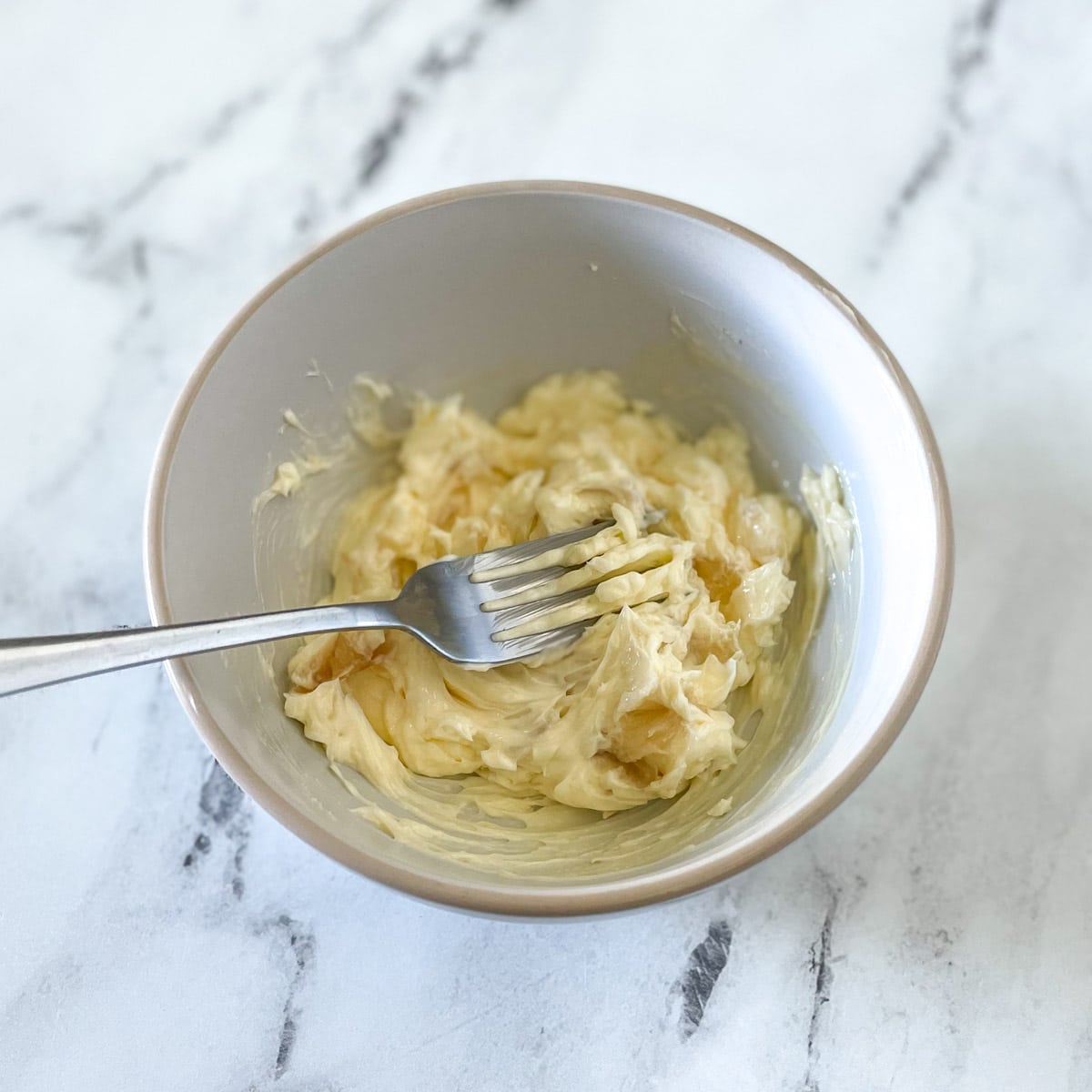 Roasted garlic is smashed into softened butter with a fork.
