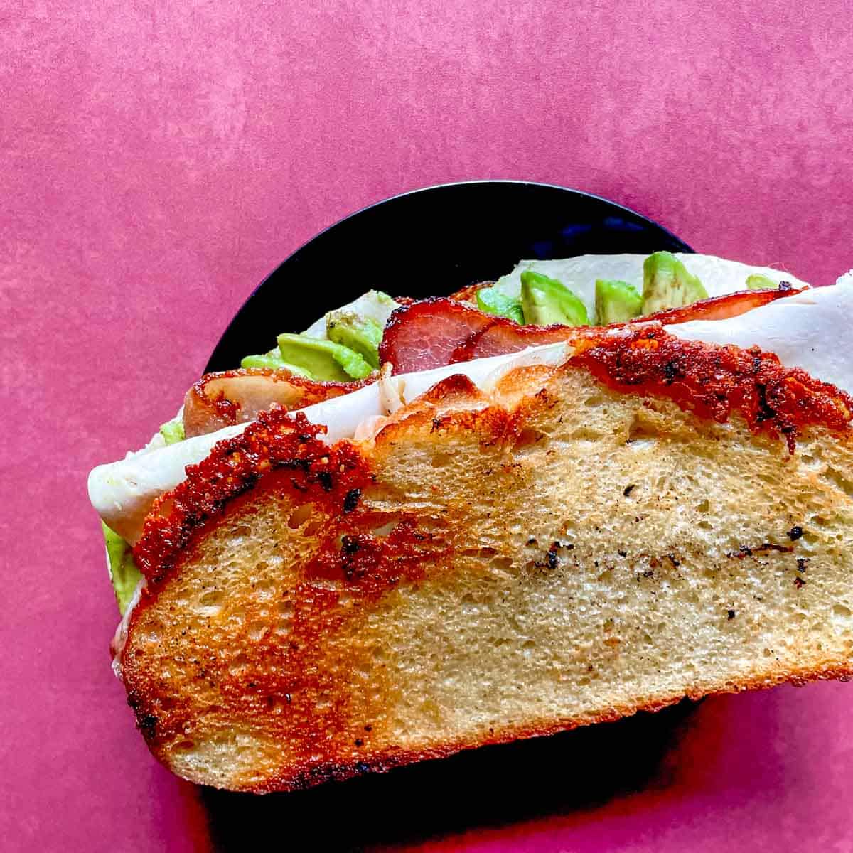 The toasted turkey avocado sandwich is shown from above on a red background.