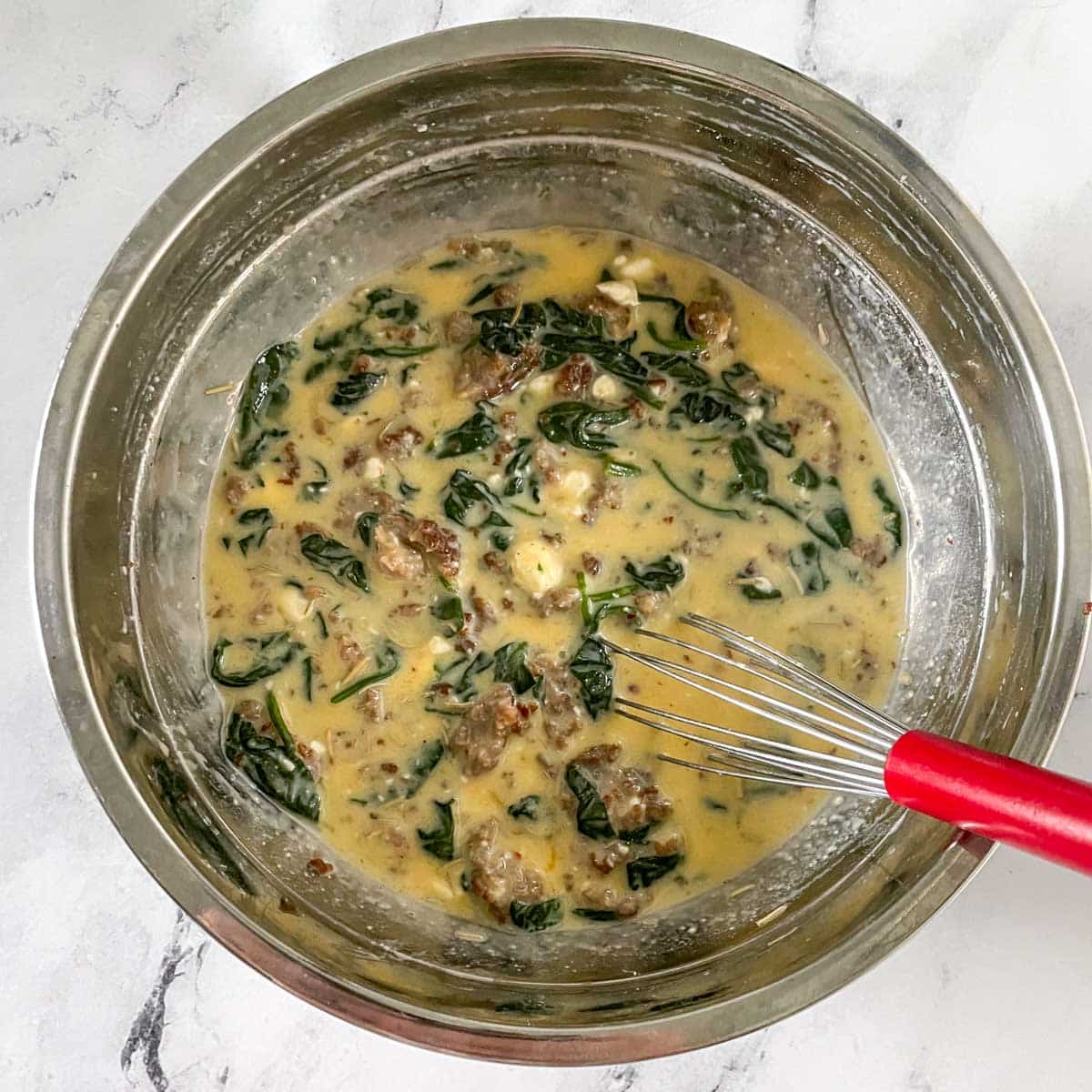 The filling for sausage spinach quiche is mixed in a bowl.
