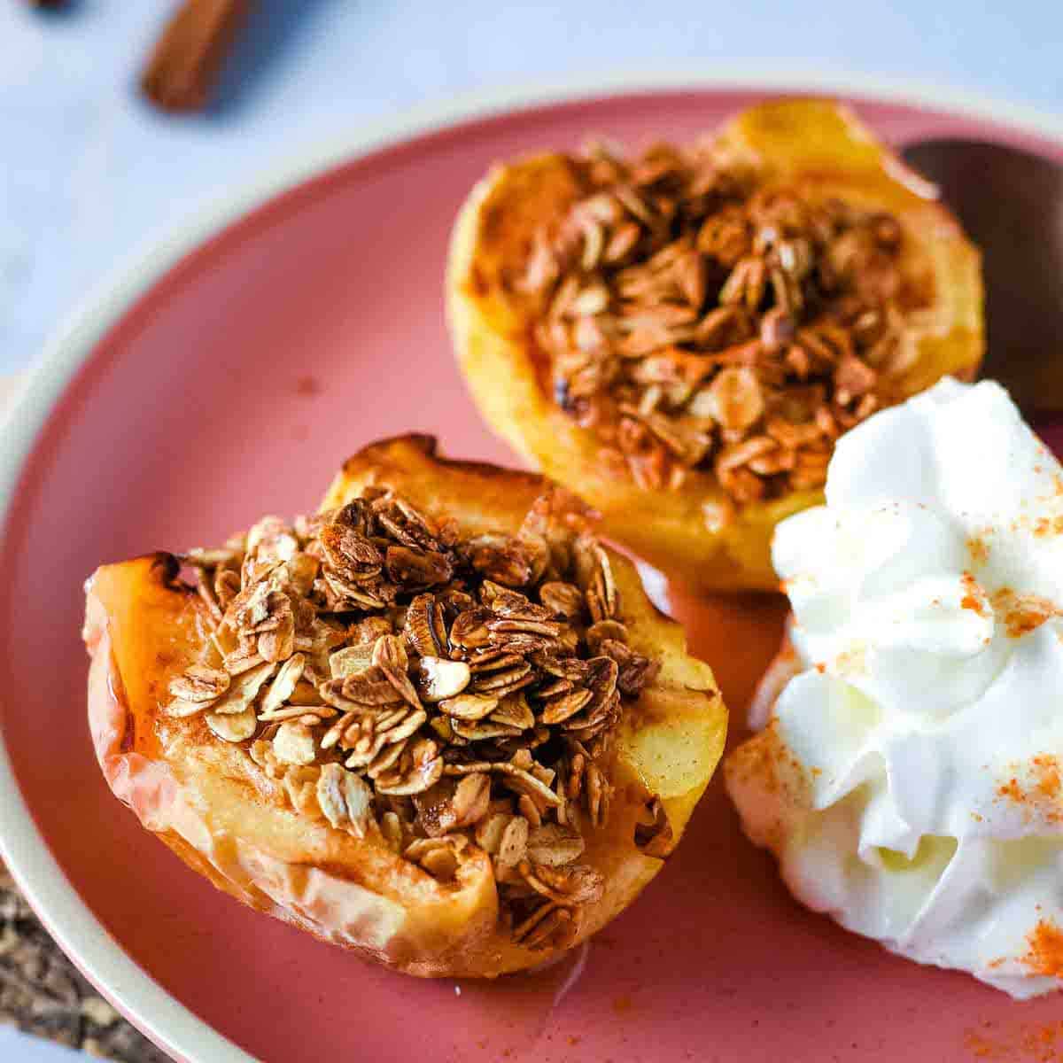 Two baked air fryer apple haves are shown on a pink plate with whipped cream.