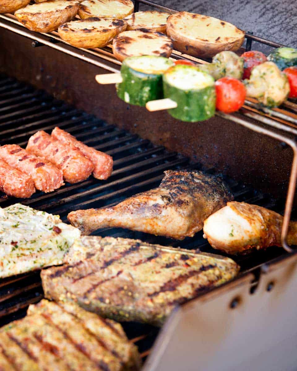 Steak, chicken, and vegetable kabobs are shown cooking on a grill.