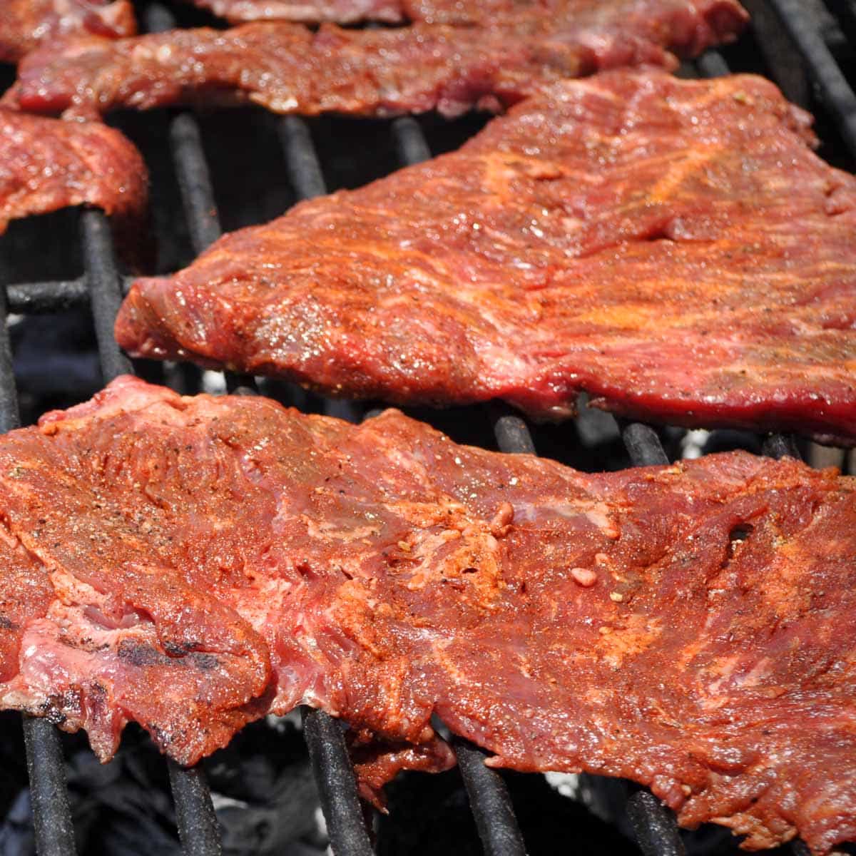 Carne asada cooks on black grill grates.