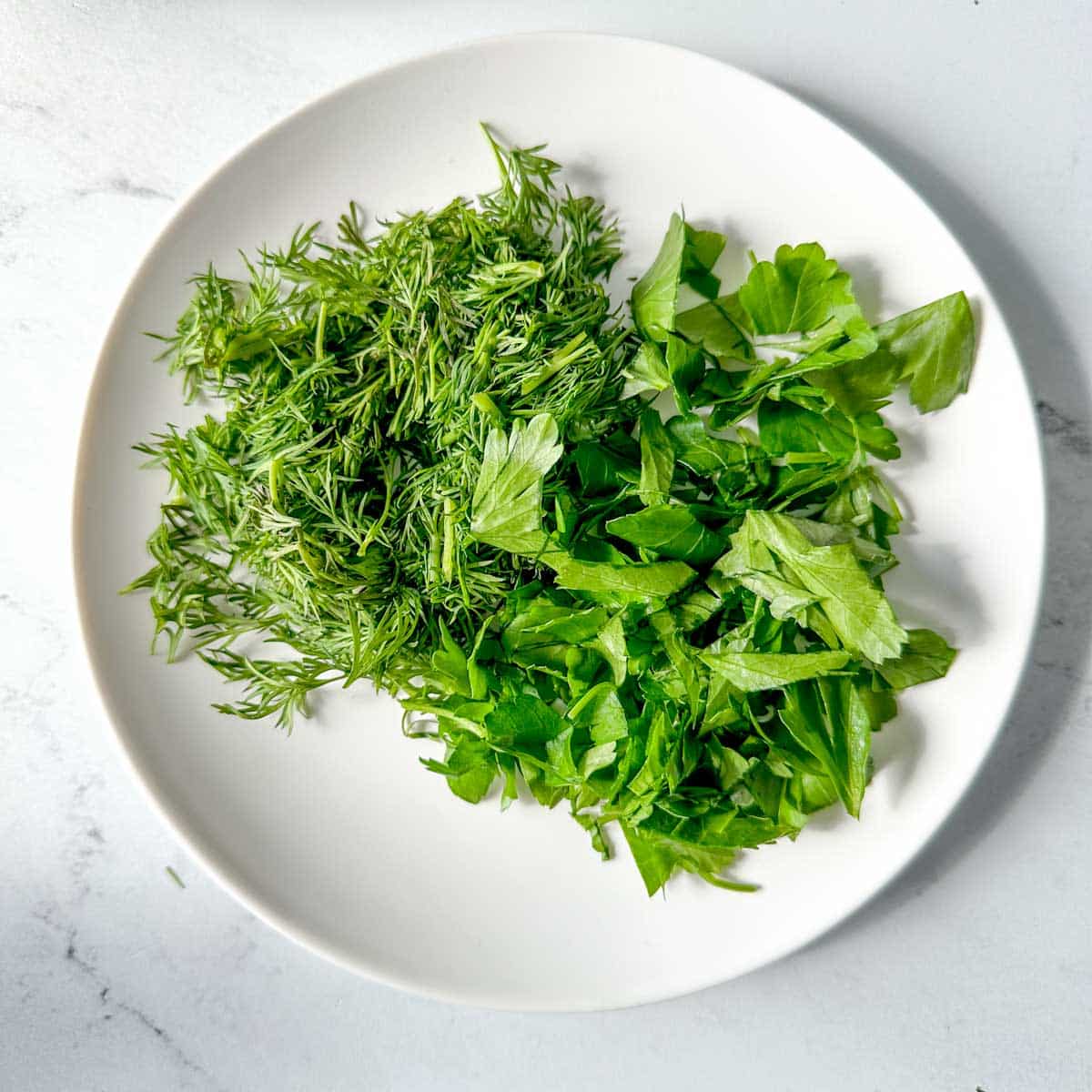 dill and parsley on a white plate/