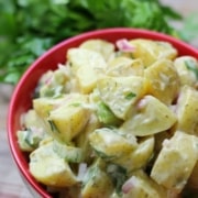 A bowl of potato salad is shown beside a bunch of parsley.