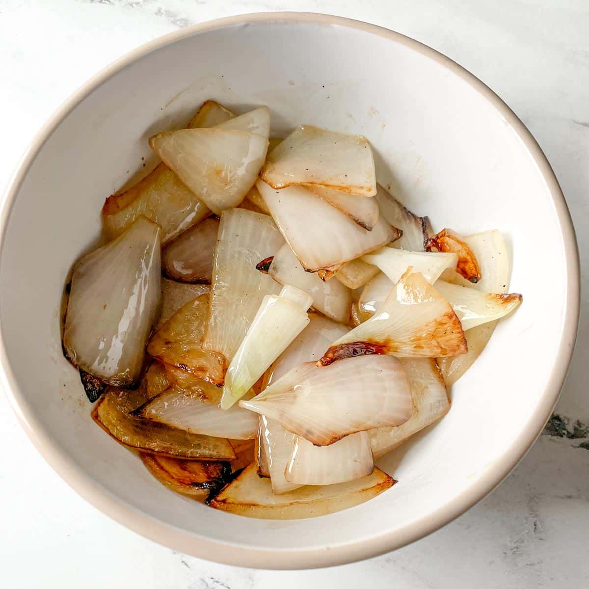 Cooked onions are shown in a white bowl.