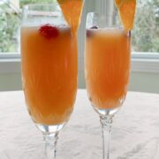 Two cranberry orange mimosas are garnished with orange slices and cranberries.
