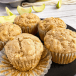 Apple muffins sit on a white wooden backdrop with apple slices.