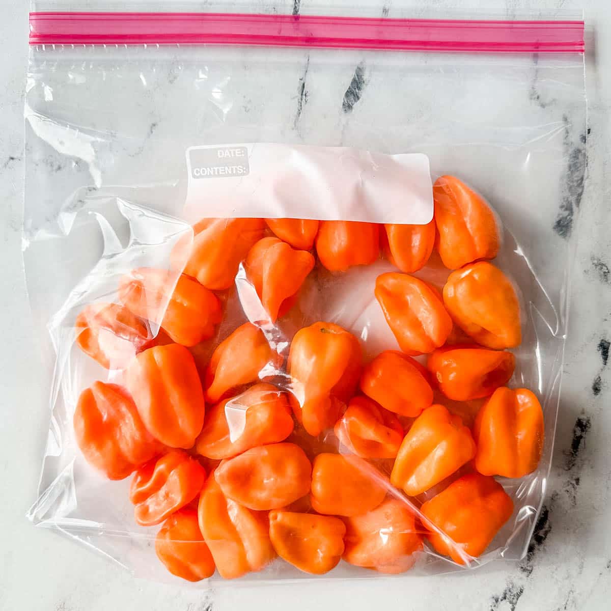 Frozen habanero peppers are shown in a freezer-safe plastic bag.