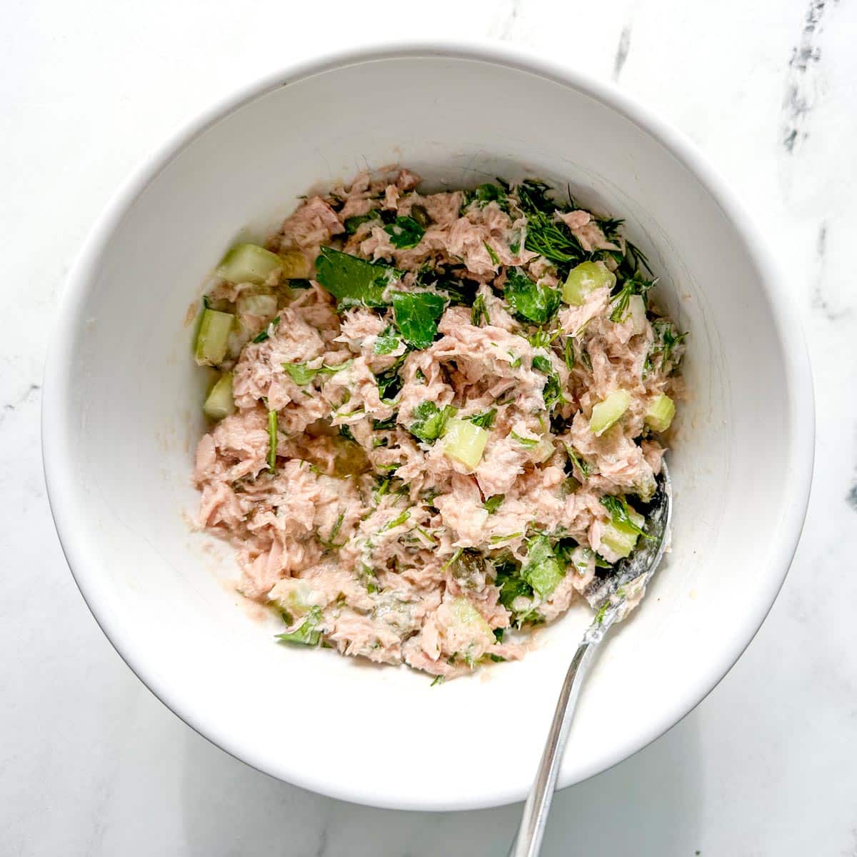 The ingredients for healthy tuna salad without mayo are mixed in a white bowl.