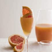 A pink grapefruit mimosa is garnished with a wedge of grapefruit.