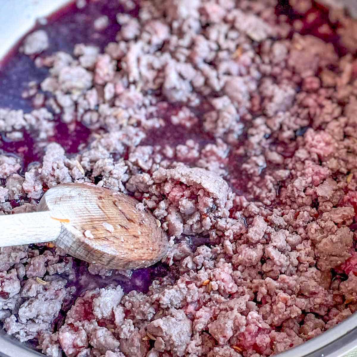 Red wine is added to the ground beef in the pan.